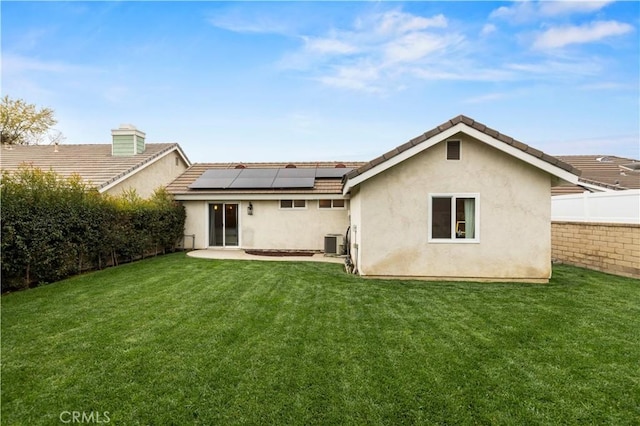 back of house with a fenced backyard, stucco siding, solar panels, central AC, and a lawn