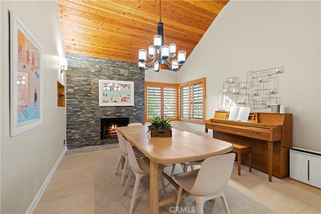 dining space with an inviting chandelier, high vaulted ceiling, a stone fireplace, and light wood-style flooring