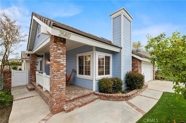 view of side of home with a chimney, covered porch, driveway, and an attached garage