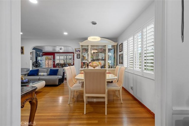 dining space with recessed lighting, arched walkways, light wood-style flooring, and baseboards