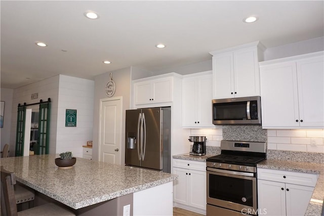 34539 Velvetleaf St, Winchester, CA 92596 - kitchen featuring appliances with stainless steel finishes, white cabinetry, light stone countertops, a breakfast bar area, and a center island