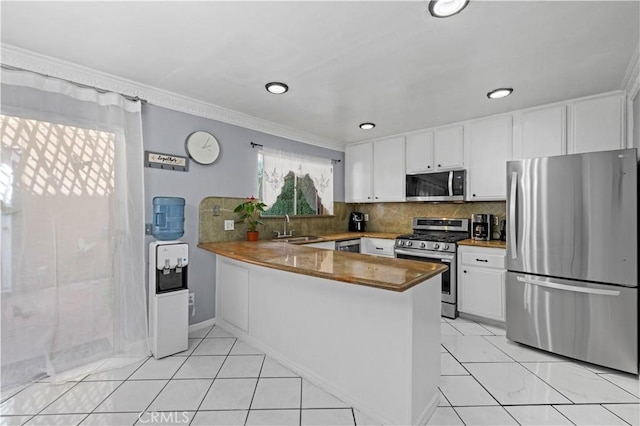 kitchen with a peninsula, a sink, white cabinetry, backsplash, and appliances with stainless steel finishes