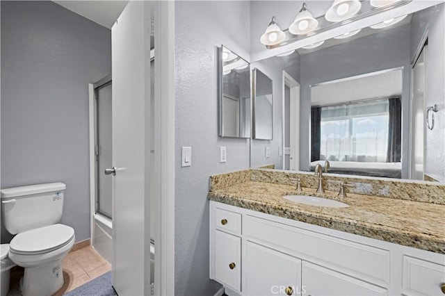 full bathroom featuring toilet, vanity, tile patterned flooring, a textured wall, and shower / bath combination with glass door