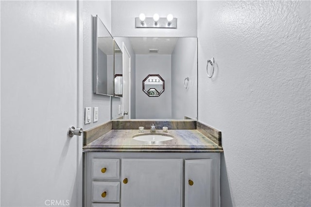 bathroom featuring vanity, a textured wall, and visible vents