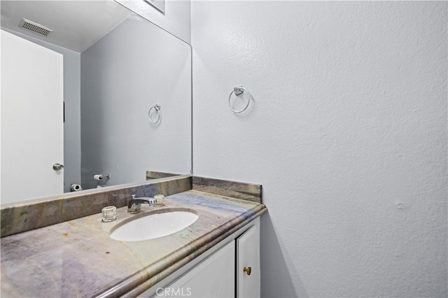 bathroom with visible vents, vanity, and a textured wall