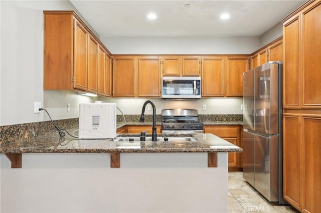 kitchen featuring a peninsula, brown cabinetry, dark stone counters, and appliances with stainless steel finishes