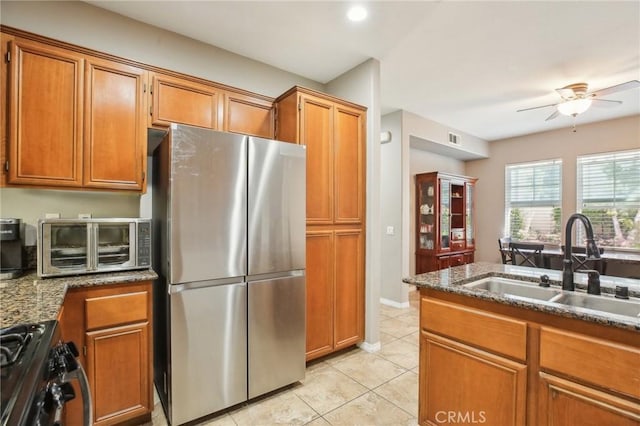 kitchen featuring a sink, ceiling fan, appliances with stainless steel finishes, brown cabinetry, and light tile patterned flooring