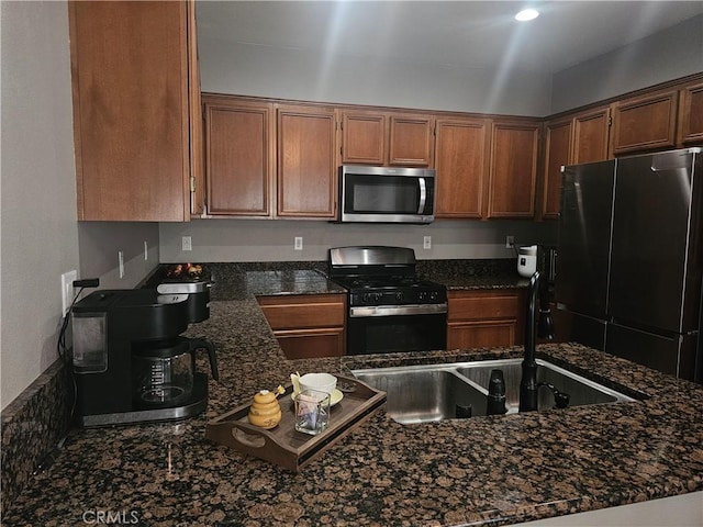 kitchen with dark stone countertops, brown cabinets, a sink, and black appliances