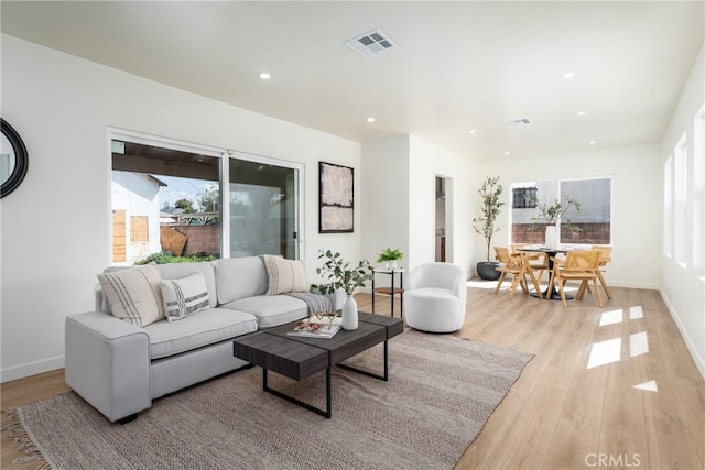 living room featuring light wood finished floors, baseboards, visible vents, and a healthy amount of sunlight