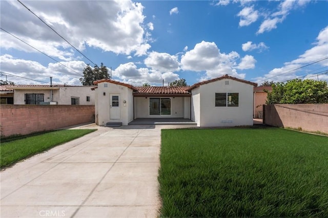 back of house with stucco siding, driveway, fence, and a yard