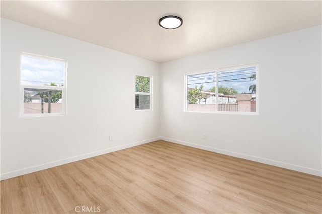 empty room with plenty of natural light, baseboards, and light wood finished floors