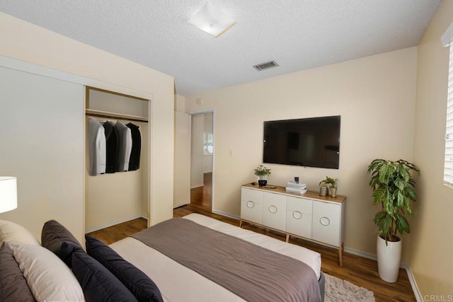 bedroom with a closet, a textured ceiling, visible vents, baseboards, and wood finished floors