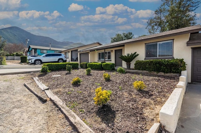ranch-style house with stucco siding, an attached garage, a mountain view, and driveway