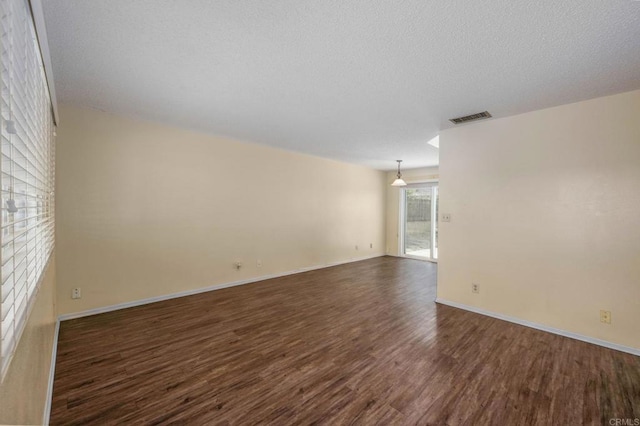 unfurnished room featuring visible vents, a textured ceiling, baseboards, and dark wood finished floors