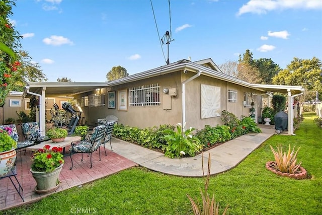 rear view of house featuring a lawn, a patio area, and stucco siding