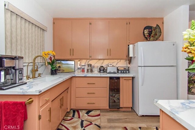 kitchen featuring wine cooler, a sink, freestanding refrigerator, light wood-style floors, and light countertops
