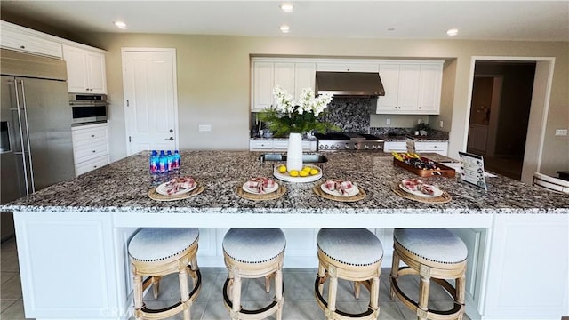 105 Tinker, Irvine, CA 92618 - kitchen with under cabinet range hood, stainless steel appliances, white cabinets, dark stone countertops, and a large island with sink