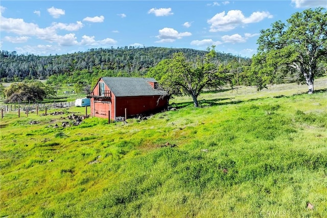 view of yard featuring a wooded view, an outbuilding, and a rural view