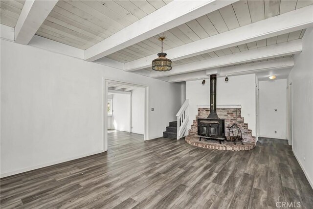 living area featuring stairs, a wood stove, baseboards, beam ceiling, and wood finished floors