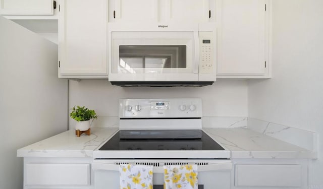 kitchen featuring white cabinets, light stone counters, and white appliances