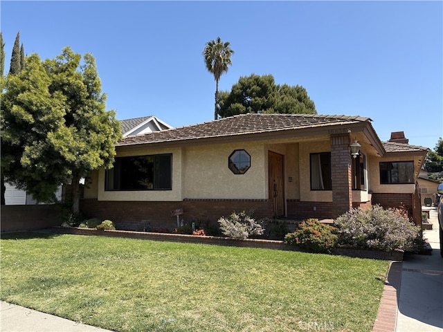 view of front facade featuring brick siding, a front yard, and stucco siding