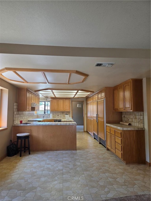 kitchen with decorative backsplash, tile countertops, a peninsula, and visible vents