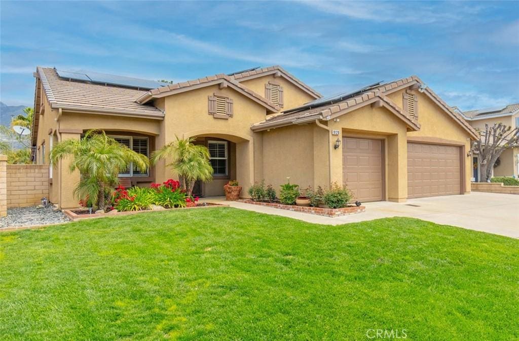 9120 Hamilton St, Rancho Cucamonga, CA 91701 - mediterranean / spanish-style house featuring a front yard, stucco siding, an attached garage, and roof mounted solar panels