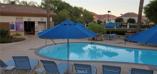 pool at dusk featuring fence, a mountain view, a patio, and a community pool