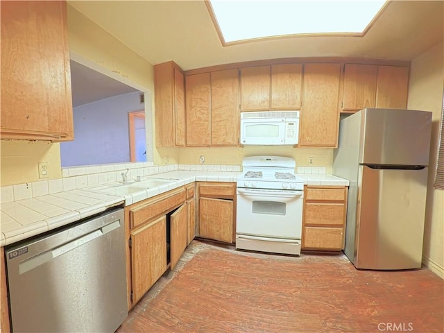 kitchen featuring light wood-style flooring, tile counters, stainless steel appliances, and a sink