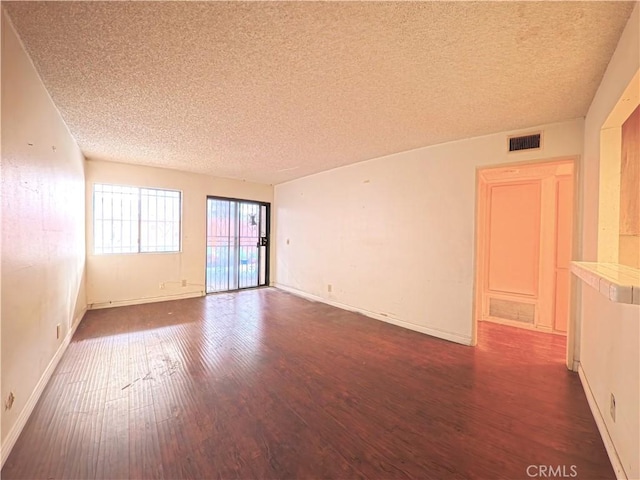 spare room featuring baseboards, visible vents, a textured ceiling, and dark wood-style flooring