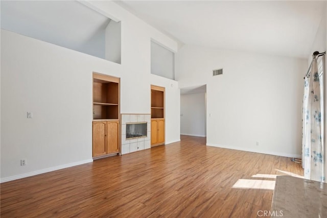 unfurnished living room featuring high vaulted ceiling, baseboards, built in shelves, visible vents, and wood finished floors