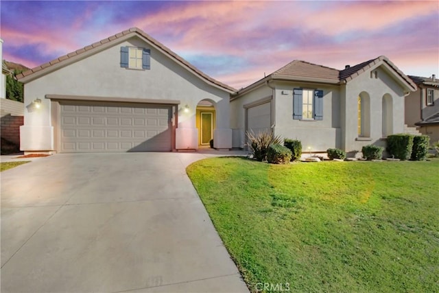 mediterranean / spanish house with a garage, stucco siding, concrete driveway, a lawn, and a tiled roof