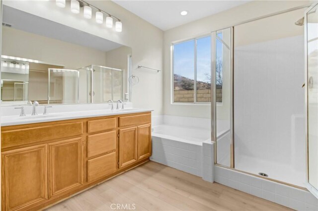 full bath featuring double vanity, wood finished floors, a bath, a sink, and a stall shower