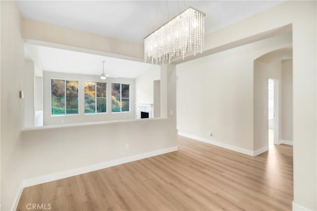 unfurnished living room with baseboards, wood finished floors, ceiling fan with notable chandelier, and a fireplace