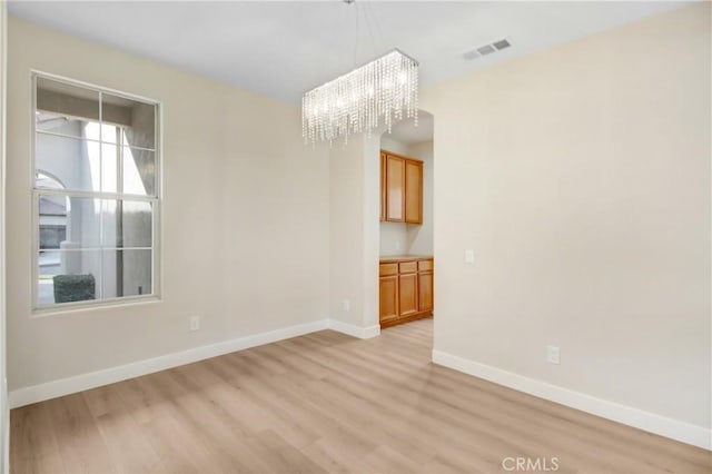 empty room with baseboards, a notable chandelier, visible vents, and light wood-style floors