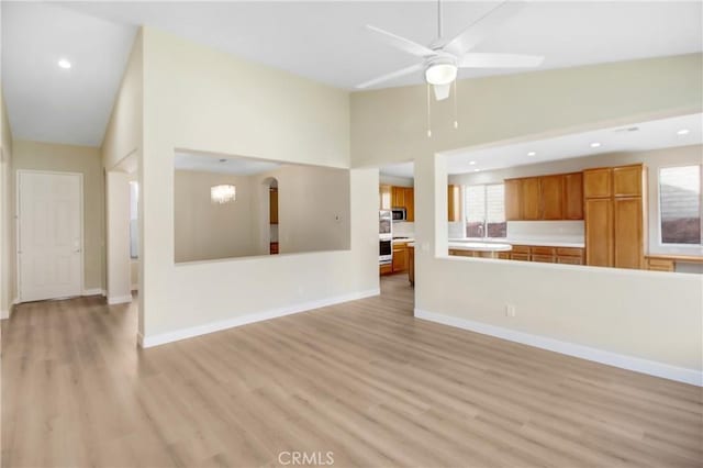 unfurnished living room featuring a ceiling fan, baseboards, light wood finished floors, and high vaulted ceiling