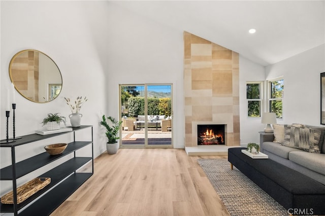 living area featuring high vaulted ceiling, plenty of natural light, light wood-style floors, and a tiled fireplace