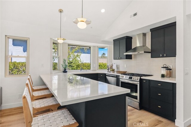 kitchen with wall chimney range hood, dark cabinetry, visible vents, and stainless steel appliances