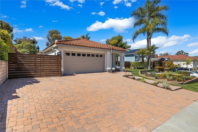 mediterranean / spanish home featuring stucco siding, decorative driveway, a garage, a tiled roof, and fence