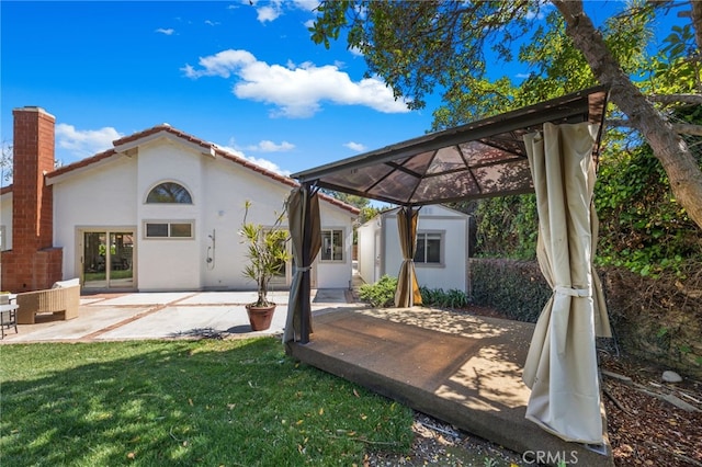 rear view of property featuring a tiled roof, a lawn, a chimney, a patio, and an outbuilding