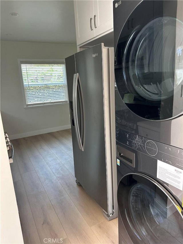 washroom featuring stacked washer and clothes dryer, cabinet space, baseboards, and light wood finished floors
