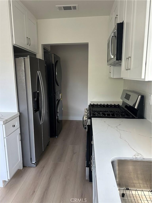 kitchen with stainless steel appliances, light stone counters, light wood finished floors, visible vents, and white cabinets