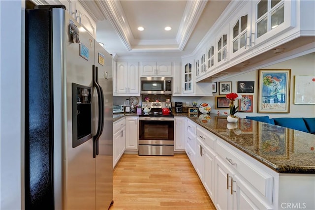 kitchen with a peninsula, light wood-style flooring, crown molding, a tray ceiling, and appliances with stainless steel finishes