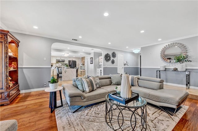 living room with crown molding, recessed lighting, arched walkways, light wood finished floors, and visible vents