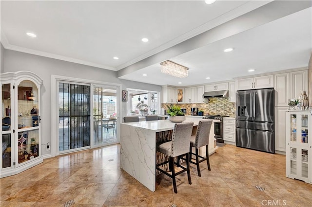 kitchen featuring a kitchen bar, tasteful backsplash, ornamental molding, stainless steel appliances, and under cabinet range hood