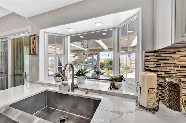 interior space with backsplash, marble finish floor, a sink, and light stone counters