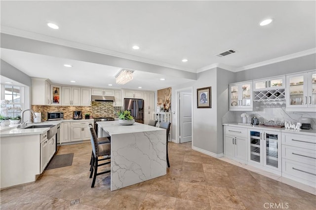 kitchen featuring visible vents, stainless steel appliances, tasteful backsplash, under cabinet range hood, and a breakfast bar area