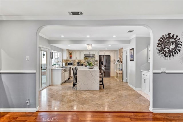 dining space with ornamental molding, baseboards, arched walkways, visible vents, and light wood-style flooring