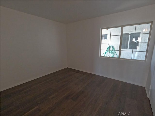 spare room with baseboards and dark wood-style floors