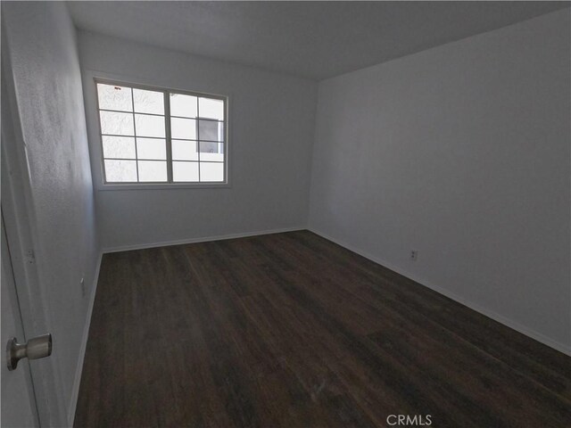 spare room featuring baseboards and dark wood-style flooring